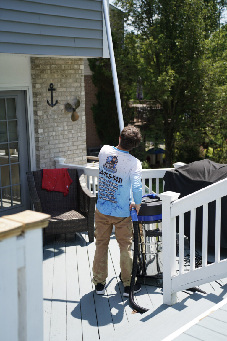 Professional gutter cleaning in Carnegie, PA with technician using a vacuum pole system from a deck to clear second-story gutters.