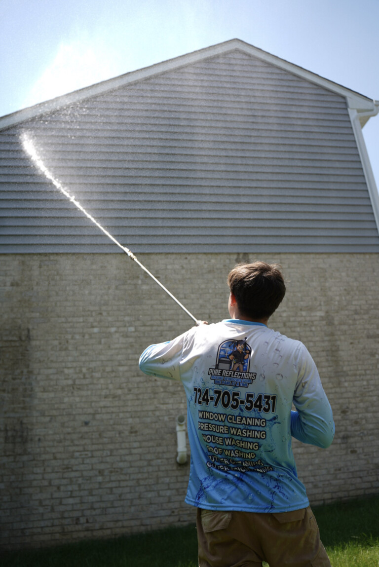 Exterior house washing in Presto, PA with low-pressure soft wash system removing algae from upper vinyl siding.