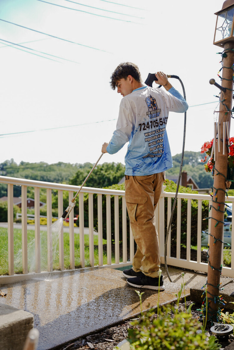 Pure Reflections technician pressure washing a concrete porch and railing at a home in Monroeville, PA.