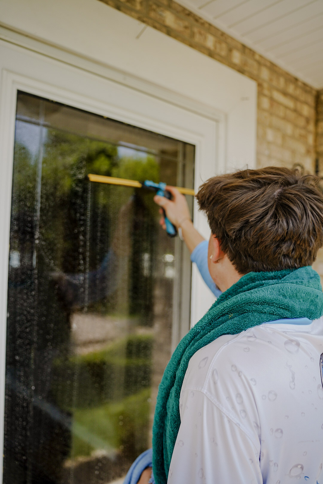 Pure Reflections technician providing residential window cleaning service in Imperial, PA cleaning exterior glass door with squeegee.